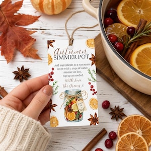 May include: A rectangular white paper tag with brown twine featuring the text Autumn SIMMER POT, instructions to add ingredients to a saucepan with 2 cups of water, and a graphic of a mason jar filled with dried orange slices, cinnamon, and berries.
