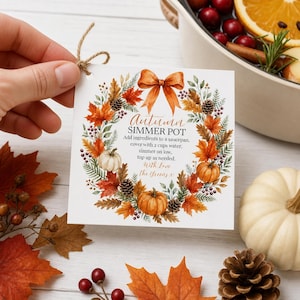 May include: A square white gift tag with a twine loop featuring a watercolour wreath of autumn leaves, pinecones, berries, and pumpkins. The text reads: Autumn SIMMER POT, Add ingredients to a saucepan, cover with 2 cups water, simmer on low, top up as needed, With Love The Greens x.