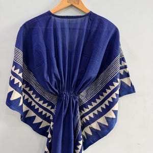 May include: A deep blue kaftan featuring a white geometric pattern along the edges and sleeves. The garment has a cinched waist with a drawstring detail, a V-neckline, and wide, flowing sleeves that drape from the shoulders in a loose silhouette.