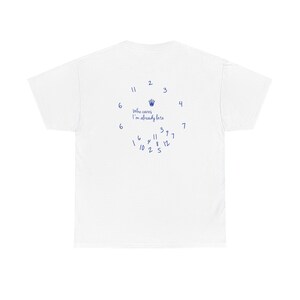 May include: White t-shirt with a blue clock design and the text "Who cares, I'm already late." The clock's numbers are scattered around the shirt's back, with a hand symbol at the top. A casual, humorous design.