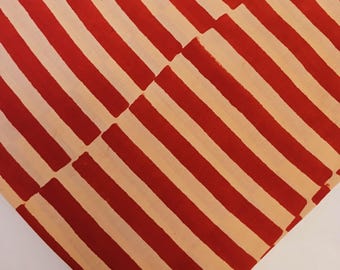May include: A piece of fabric featuring a repeating pattern of bold, diagonal red stripes set against a light beige background. The stripes are arranged in two distinct sections that meet at a central diagonal seam, creating a chevron-like effect.