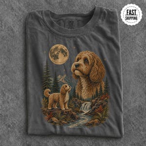 May include: A charcoal grey t-shirt featuring a graphic print of a golden-brown doodle dog standing on a rocky ledge near a waterfall and pine trees, with a large full moon in the night sky above a larger portrait of the same dog breed.