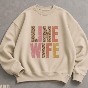 May include: A beige crewneck sweatshirt featuring the text "LINE WIFE" printed in a block font. The letters alternate between a brown leopard print pattern and solid distressed colors including muted pink, terracotta, and mustard yellow.