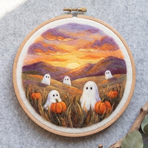 Puede incluir: Una pieza de arte en bastidor de bordado con lana fieltrada que muestra un paisaje al atardecer con nubes moradas y naranjas sobre colinas. Cinco figuras de fantasmas blancos con ojos negros se sitúan en un campo de hierba alta y calabazas.