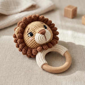 Puede incluir: Un sonajero de bebé con forma de león hecho a ganchillo. El león tiene una cara beige, una melena marrón, ojos negros y mejillas rosas. El mango es un anillo de ganchillo blanco. El sonajero está hecho de hilo suave y madera.
