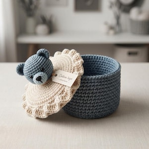 May include: A round, blue crocheted basket with a matching lid. The lid features a cream-colored, ruffled crocheted edge and a blue crocheted bear head attached to the top. A small, rectangular paper tag attached to the bear reads Cotton tape.