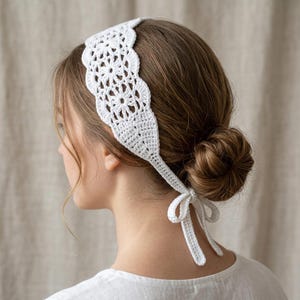 May include: A white crochet headband featuring a repeating floral pattern with scalloped edges. The headband is constructed from thin white yarn and includes two long, narrow ties at the back that are knotted into a bow to secure the accessory.