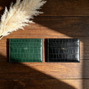 May include: Two rectangular card holders with a crocodile-embossed texture. The left holder is dark green with the letters GB embossed in gold, and the right holder is black with the letters DG embossed in gold, each featuring multiple slots.