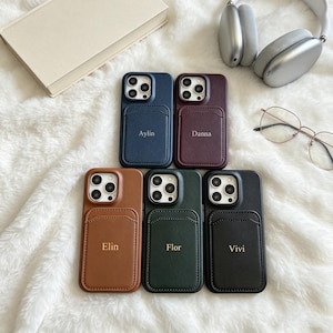 Könnte beinhalten: Fünf Smartphone-Hüllen in Lederoptik mit integriertem Kartenfach, jeweils mit einem in Gold geprägten Namen: Aylin, Danna, Elin, Flor und Vivi. Die Hüllen sind in Marineblau, Bordeaux, Hellbraun, Waldgrün und Schwarz gehalten.