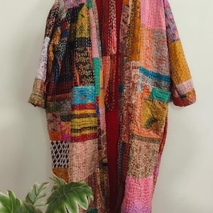 Può includere: Una giacca a maniche lunghe in stile kimono caratterizzata da un design patchwork di vari tessuti colorati con intricati motivi di cucitura. Il capo presenta una fodera interna rossa a tinta unita, un'apertura frontale e due grandi tasche.
