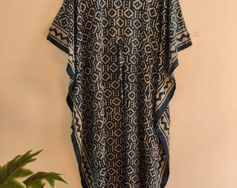 Könnte beinhalten: Ein locker sitzendes Kaftan-Kleid mit einem geometrischen Blockdruckmuster in Dunkelblau und Cremeweiß. Das Kleidungsstück hat weite, kurze Ärmel, einen V-Ausschnitt und ein mittiges Zugband in der Taille und hängt an einem Holzkleiderbügel.