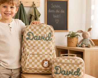 May include: A beige and white checkered backpack and matching lunch bag, both featuring the name David embroidered in green script. The backpack includes a small circular patch with a white bear illustration on the front pocket.