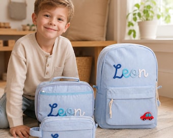 May include: A light blue corduroy backpack, lunch bag, and pencil case set. Each item features the name Leon in blue and white cursive lettering. The backpack includes a small red car applique on the front pocket and white rope zipper pulls.
