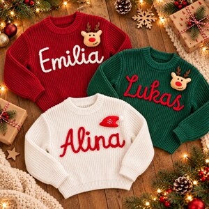 May include: Three long-sleeved knit sweaters in red, green, and white. The red sweater features the name Emilia and a reindeer applique. The green sweater features the name Lukas and a reindeer applique. The white sweater features the name Alina and a red Santa hat applique.