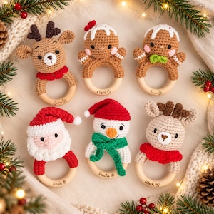 May include: Six crocheted baby rattles featuring a reindeer, two gingerbread figures, Santa Claus, a snowman, and another reindeer. Each toy is attached to a smooth wooden ring engraved with names including Lukas, Clara, Timon, Froh, Paula, and Weih.
