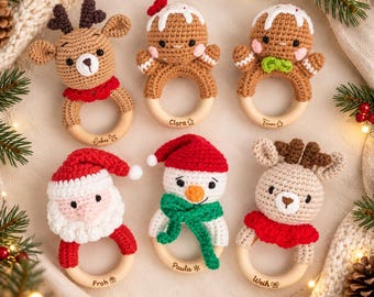 May include: Six crocheted baby rattles featuring a reindeer, two gingerbread figures, Santa Claus, and a snowman, each attached to a smooth wooden ring. The wooden rings are engraved with the names Lukas, Clara, Timon, Froh, Paula, and Weih.