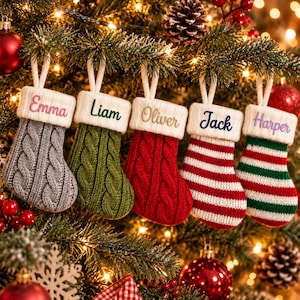 May include: Five knit Christmas stockings hanging from a tree, each with a white cuff embroidered with names: Emma in pink, Liam in green, Oliver in gold, Jack in blue, and Harper in purple. The stockings feature cable knit and striped patterns.