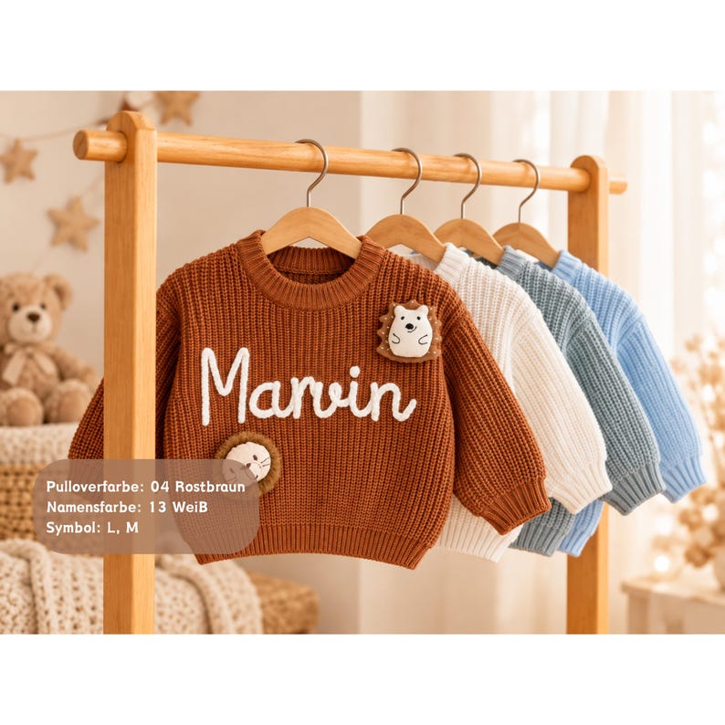 May include: A rust-brown knitted sweater featuring the white embroidered name Marvin, a hedgehog patch, and a lion patch. Behind it hang three additional sweaters in white, light blue, and a slightly darker blue on wooden hangers.