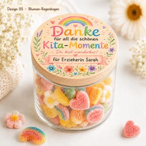 May include: A clear glass jar filled with colorful sugar-coated gummy candies in shapes of hearts, flowers, and rainbows. The wooden lid features a printed design with a rainbow, floral accents, and the German text Danke f&uuml;r alle Kita-Momente.