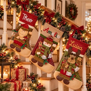 May include: Three Christmas stockings hanging on a staircase railing. The left stocking features a Santa Claus and the name Theo. The middle stocking features a snowman and the name Amelie. The right stocking features a reindeer and the name Luisa.