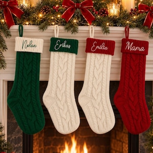 May include: Four cable-knit Christmas stockings hanging in a row. The first is green with a white cuff labeled Nolan, the second is white with a green cuff labeled Erikas, the third is white with a red cuff labeled Emilia, and the fourth is red with a red cuff labeled Mama.