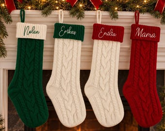 May include: Four cable-knit Christmas stockings hanging in a row. The first is green with a white cuff labeled Nolan, the second is white with a green cuff labeled Erikas, the third is white with a red cuff labeled Emilia, and the fourth is red with a red cuff labeled Mama.