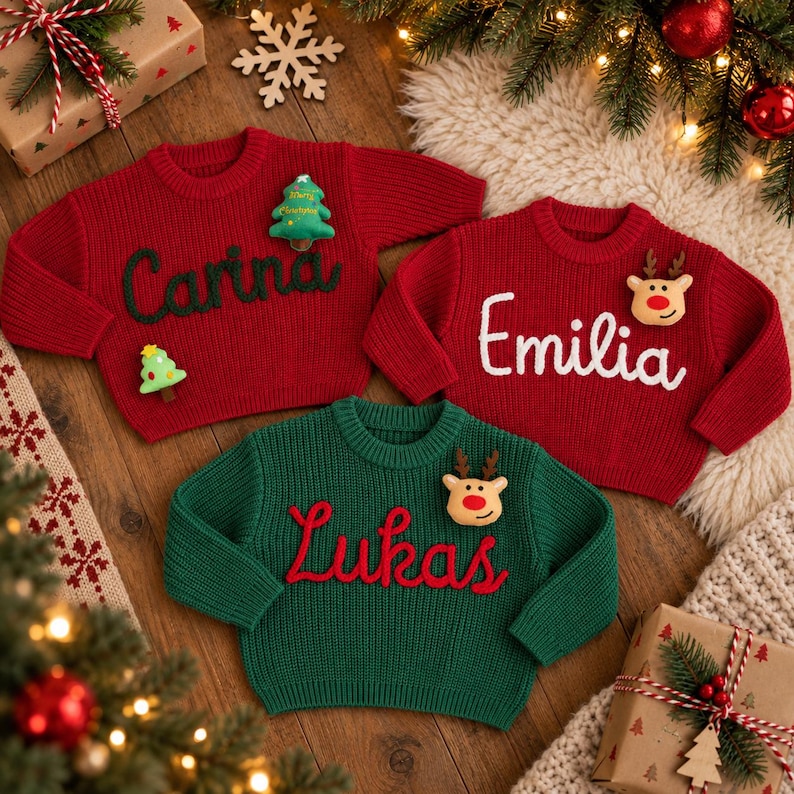 May include: Three knitted sweaters in red and green with long sleeves and crew necks. Two red sweaters feature the names Carina in green and Emilia in white, while the green sweater features the name Lukas in red, with festive appliques.