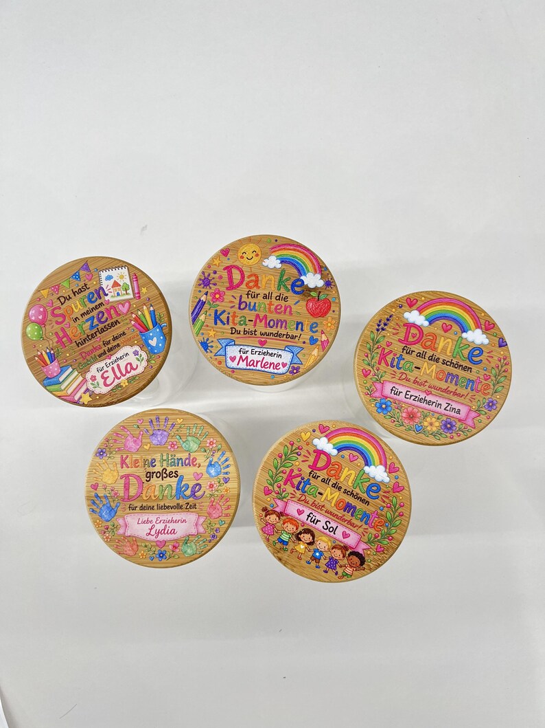 Puede incluir: Cinco tapas redondas de madera para frascos con dise&ntilde;os impresos coloridos, texto en alem&aacute;n, arco&iacute;ris, flores y &uacute;tiles escolares. Cada tapa est&aacute; personalizada con un nombre, incluyendo Ella, Marlene, Zina, Lydia y Sol, para docentes.