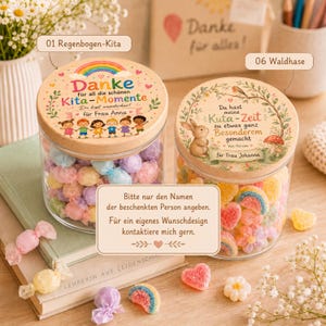 Puede incluir: Dos frascos de vidrio transparente con tapas de madera llenos de dulces coloridos. La tapa izquierda presenta una ilustraci&oacute;n de un arco&iacute;ris y ni&ntilde;os con el texto 'Danke f&uuml;r all die sch&ouml;nen Kita-Momente'.
