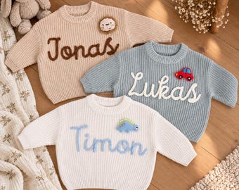 May include: Three long-sleeve knit sweaters in beige, light blue, and white. The beige sweater features the name Jonas and a lion patch. The light blue sweater displays the name Lukas and a red car patch. The white sweater shows the name Timon and a blue dinosaur patch.