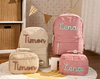 May include: Two corduroy backpacks and two matching lunch bags in dusty pink and beige. The pink set features the name Lena in teal script, while the beige set features the name Timon in brown script. Each bag has a front zippered pocket.
