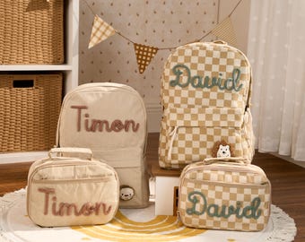 May include: Two backpacks and two lunch bags in beige and white. One set is solid beige with the name Timon in brown script. The other set features a beige and white checkerboard pattern with the name David in green script and a small hedgehog patch.