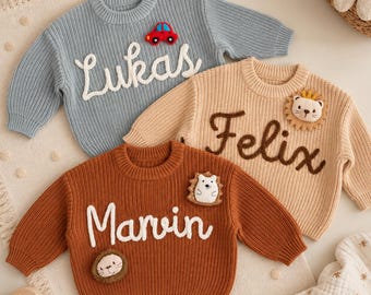 May include: Three long-sleeve knit sweaters in light blue, beige, and rust orange. The blue sweater features the name Lukas and a red car patch. The beige sweater features the name Felix and a lion patch. The rust sweater features the name Marvin, a hedgehog patch, and a lion patch.