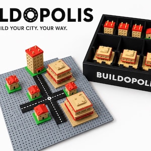 Puede incluir: Un sistema de construcción de ciudad modular titulado BUILDOPOLIS que incluye una placa base de rejilla gris, segmentos de carretera negros y edificios en miniatura de color canela con techos rojos. Una caja negra con el texto BUILDOPOLIS.