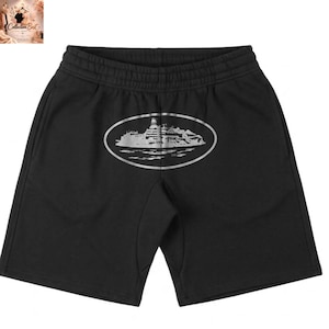 May include: Black shorts with an elastic waistband and a silver graphic of a building on an island within an oval frame. The shorts are made of a soft material and have a casual style.