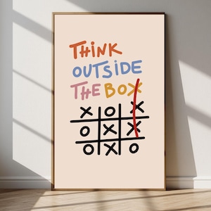 以下が含まれることがあります： ライトベージュの背景に「THINK OUTSIDE THE BOX」というオレンジ、青、ピンクの文字が描かれた額装アートプリント。テキストの下には、XとOのマークが入った黒い三目並べのグリッドがあり、右側の列には赤い縦線が引かれています。