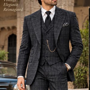 May include: A dark charcoal grey plaid three-piece suit featuring a blazer, a vest with a gold pocket watch chain, and matching trousers. The ensemble includes a white dress shirt, a black tie, and a pocket square. Text reads SharmasBespokeJaipur.