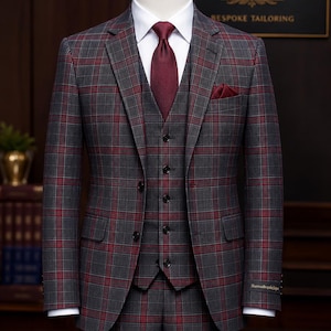 May include: A three-piece suit in a grey and red plaid pattern, featuring a blazer, a five-button vest, and trousers. The suit is worn with a crisp white collared shirt, a solid dark red necktie, and a matching red pocket square in the chest pocket.