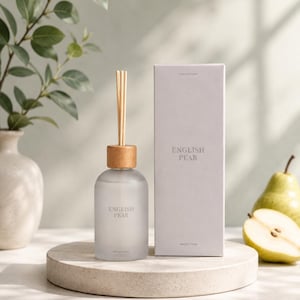 Könnte beinhalten: Ein Diffusor aus Milchglas mit einem hellen Holzdeckel und mehreren Holzstäbchen, begleitet von einer passenden rechteckigen Schachtel. Sowohl die Flasche als auch die Schachtel sind mit dem Text English Pear und Breeze Town in Grau beschriftet.
