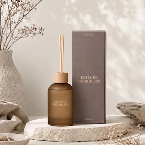 May include: A brown frosted glass reed diffuser bottle with a light wood cap and several reeds, accompanied by a matching rectangular brown box. Both the bottle and the box feature the text EXPLORE BOUNDLESS in a clean, gold-toned font.