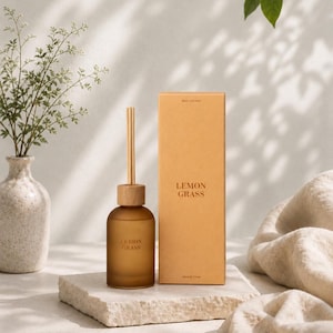 Könnte beinhalten: Ein Diffusor aus Milchglas mit einem hellen Holzdeckel und drei Stäbchen, begleitet von einer passenden rechteckigen Pappschachtel. Sowohl die Flasche als auch die Schachtel sind mit dem Text LEMON GRASS in einer schlichten, braunen Schrift versehen.