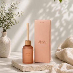 May include: A peach-colored reed diffuser set featuring a frosted glass bottle with a wooden cap and a single reed, accompanied by a matching rectangular cardboard box. Both the bottle and the box are printed with the text PEACH OOLONG.