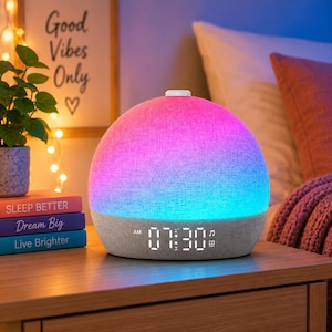 May include: A dome-shaped alarm clock with a fabric-covered exterior that glows with a gradient of pink, purple, and blue light. The base features a digital display showing the time 07:30 AM, along with small icons for music and an alarm setting.