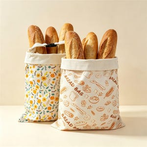 Peut inclure: Deux sacs à pain en tissu remplis de baguettes. Le sac de gauche présente un motif floral jaune et vert. Le sac de droite est blanc cassé avec des illustrations au trait marron de diverses pâtisseries et le texte BREAD BAG répété.