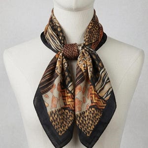 May include: A square scarf featuring a patchwork of animal prints and geometric patterns in shades of brown, tan, black, and cream. The scarf is tied in a knot at the center, displaying a black border along the edges of the fabric panels.