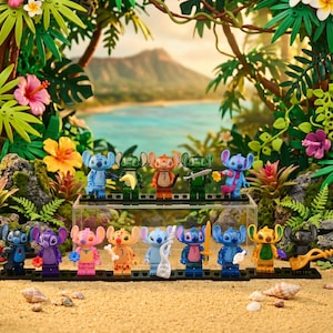 May include: A collection of colorful Stitch character figurines displayed on a sandy beach setting with tropical foliage and a scenic backdrop. Each figurine is uniquely designed, holding various accessories.