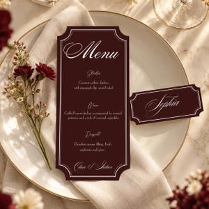 May include: A deep burgundy menu card and matching place card with white scalloped borders and elegant white script text. The menu lists courses including coconut cashew chicken, grilled lemon chicken, and chocolate mousse, signed Clara & Julian.