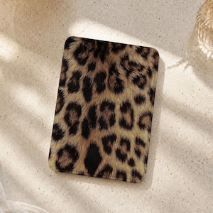 Pode incluir: Uma capa retangular para leitor eletrônico com um padrão realista de estampa de leopardo em tons de castanho, bege e preto. A capa tem cantos arredondados e uma superfície plana e lisa, exibindo uma textura detalhada de pelo de animal.
