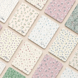 May include: A collection of rectangular tablet cases featuring various floral patterns in shades of pink, blue, green, and cream. Each case displays a personalised name in black script, including the names Lillian, Fanny, Nancy, Gladys, and Heather.