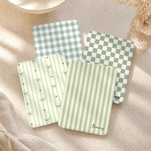 May include: Four rectangular coasters featuring sage green and white patterns including gingham, checkerboard, and vertical stripes with small bow and heart motifs. Two coasters are personalized with the names Fanny and Isabel in black script.